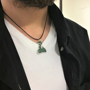 May include: A black leather cord necklace with a green and silver pendant shaped like a mythical creature.