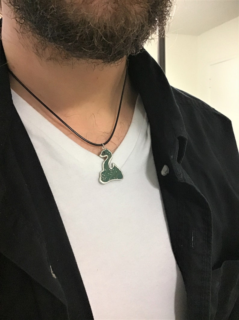 May include: A black leather cord necklace with a green and silver pendant shaped like a mythical creature.