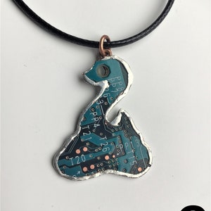 May include: A teal circuit board pendant necklace with a silver-colored frame and a copper-colored bail. The pendant is shaped like a stylized bird. The circuit board has text on it, including "PP", "T21", "T20", and "T26".