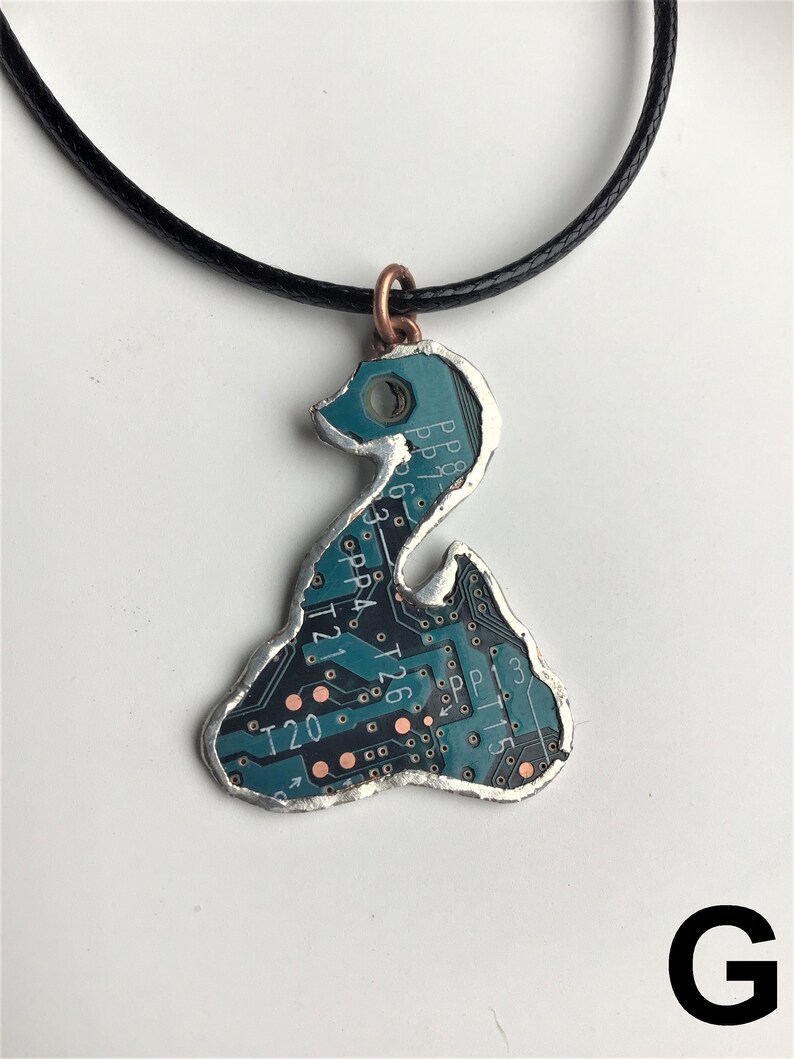 May include: A teal circuit board pendant necklace with a silver-colored frame and a copper-colored bail. The pendant is shaped like a stylized bird. The circuit board has text on it, including "PP", "T21", "T20", and "T26".