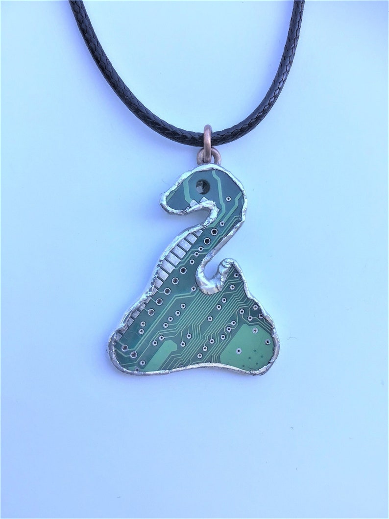 May include: A silver necklace with a green circuit board pendant shaped like a snake. The pendant is surrounded by a silver border.