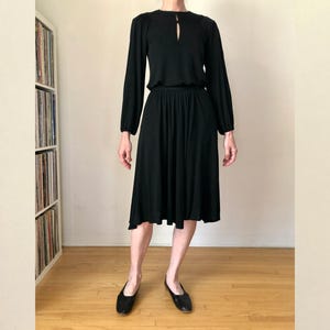 May include: A black long-sleeved dress with a keyhole neckline and a fitted bodice. The skirt is a-line and falls to the knees. The dress is made of a soft, stretchy fabric.