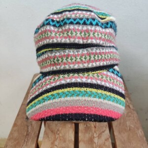 May include: A knitted hat with a folded brim, displaying a vibrant pattern of horizontal stripes. The colour palette includes pink, black, blue, green, and yellow. The hat is made from a soft, textured material, ideal for colder climates.