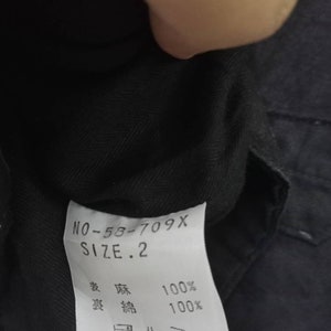 Op de afbeelding: Een zwart kledinglabel met witte tekst die "NO-58-709X SIZE. 2" en "綿 100%  綿 100%" luidt. Het label bevat ook een onderhoudsetiket met een was symbool voor 40 graden Celsius, een symbool voor verboden bleken, een strijksymbool voor lage hitte en een symbool voor verboden chemische reiniging.