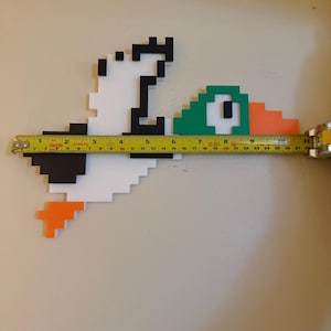 May include: A pixelated duck made of foam board, painted white, black, green, and orange. The duck is 28 inches long and is measured with a tape measure.