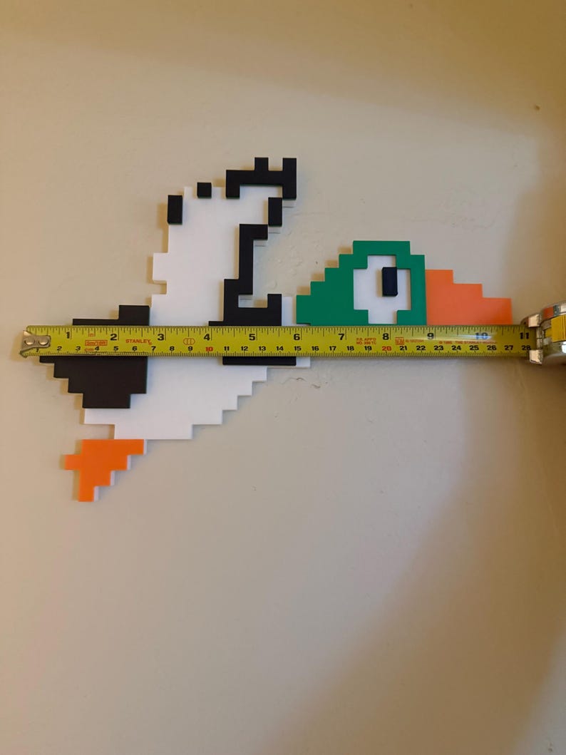 May include: A pixelated duck made of foam board, painted white, black, green, and orange. The duck is 28 inches long and is measured with a tape measure.
