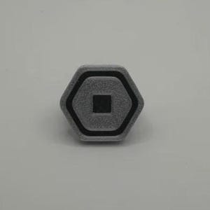 May include: A gray, hexagonal object with a black border and a black square in the center. The object has a textured surface and appears to be made of a solid material. The design is simple and geometric.