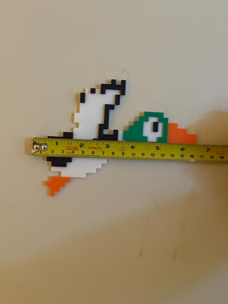 May include: A pixel art duck made of white, black, green, and orange plastic blocks. The duck is approximately 7 inches long.