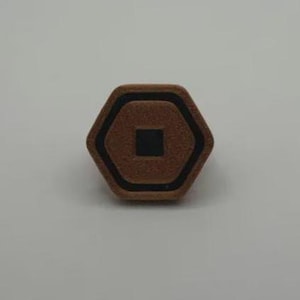 May include: A brown, hexagonal object with a black border and a black square in the center. The object has a textured surface and is set against a plain, light background.
