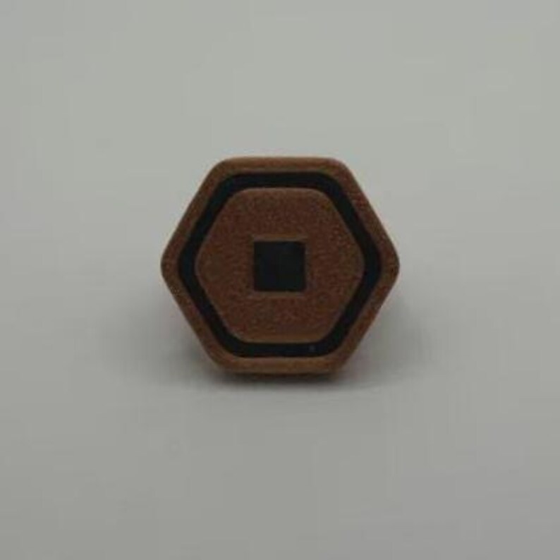 May include: A brown, hexagonal object with a black border and a black square in the center. The object has a textured surface and is set against a plain, light background.