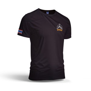 Puede incluir: Camiseta deportiva negra con un peque&ntilde;o gr&aacute;fico en el pecho y una bandera tailandesa en la manga izquierda. El gr&aacute;fico es una imagen estilizada de una persona en posici&oacute;n de combate. La camiseta est&aacute; hecha de un material ligero y transpirable.