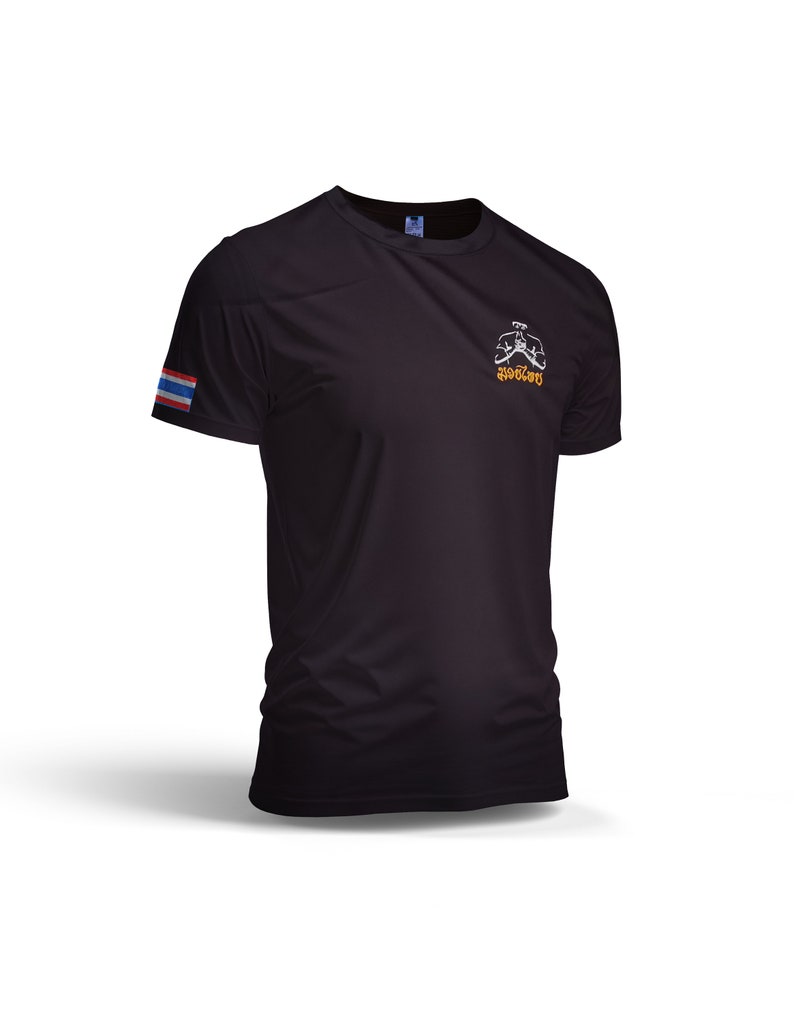 Puede incluir: Camiseta deportiva negra con un peque&ntilde;o gr&aacute;fico en el pecho y una bandera tailandesa en la manga izquierda. El gr&aacute;fico es una imagen estilizada de una persona en posici&oacute;n de combate. La camiseta est&aacute; hecha de un material ligero y transpirable.