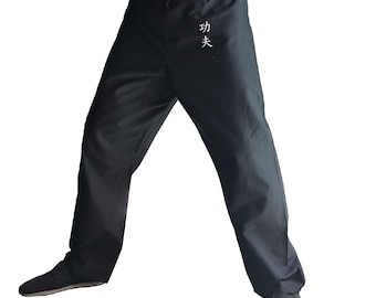 May include: Black martial arts pants with a white embroidered Chinese character on the back. The pants have a drawstring waistband and a relaxed fit.
