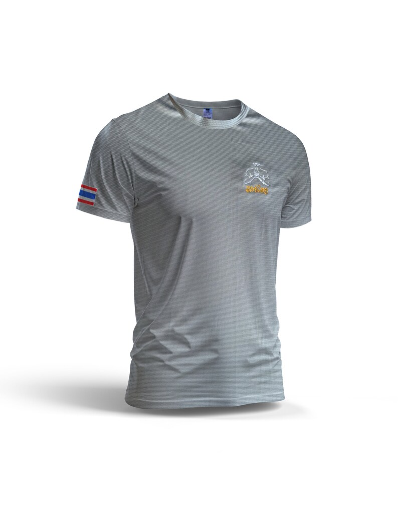 Puede incluir: Una camiseta gris de manga corta con un sutil patr&oacute;n texturizado. La camiseta presenta una peque&ntilde;a bandera tailandesa en la manga izquierda y un logotipo con texto en el pecho. La camiseta se muestra sobre un fondo blanco.