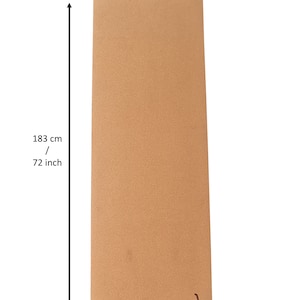 Op de afbeelding: Een bruine kurk yogamat met het woord "TAD" in zwart gedrukt in de rechterbenedenhoek. De mat is 183 cm lang en 61 cm breed.