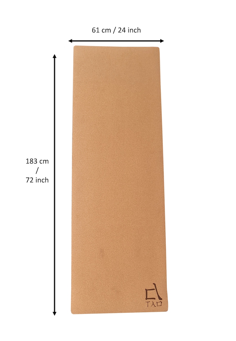 Op de afbeelding: Een bruine kurk yogamat met het woord "TAD" in zwart gedrukt in de rechterbenedenhoek. De mat is 183 cm lang en 61 cm breed.