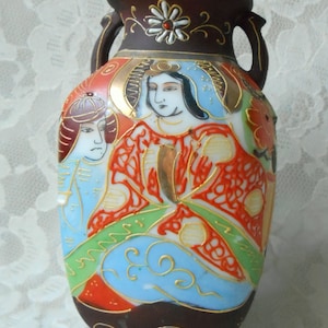 May include: A small, brown ceramic vase with two handles. The vase is decorated with a colorful Japanese-inspired design featuring figures in traditional clothing.