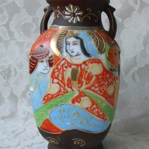 May include: A small, dark brown ceramic vase with two handles. The vase is decorated with a colorful Japanese-inspired design featuring three figures in traditional clothing. The figures are painted in shades of red, blue, green, and gold.