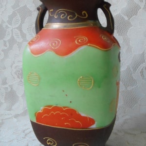 May include: A brown and green ceramic vase with gold accents and a red and orange floral design. The vase has two handles and a rounded base.