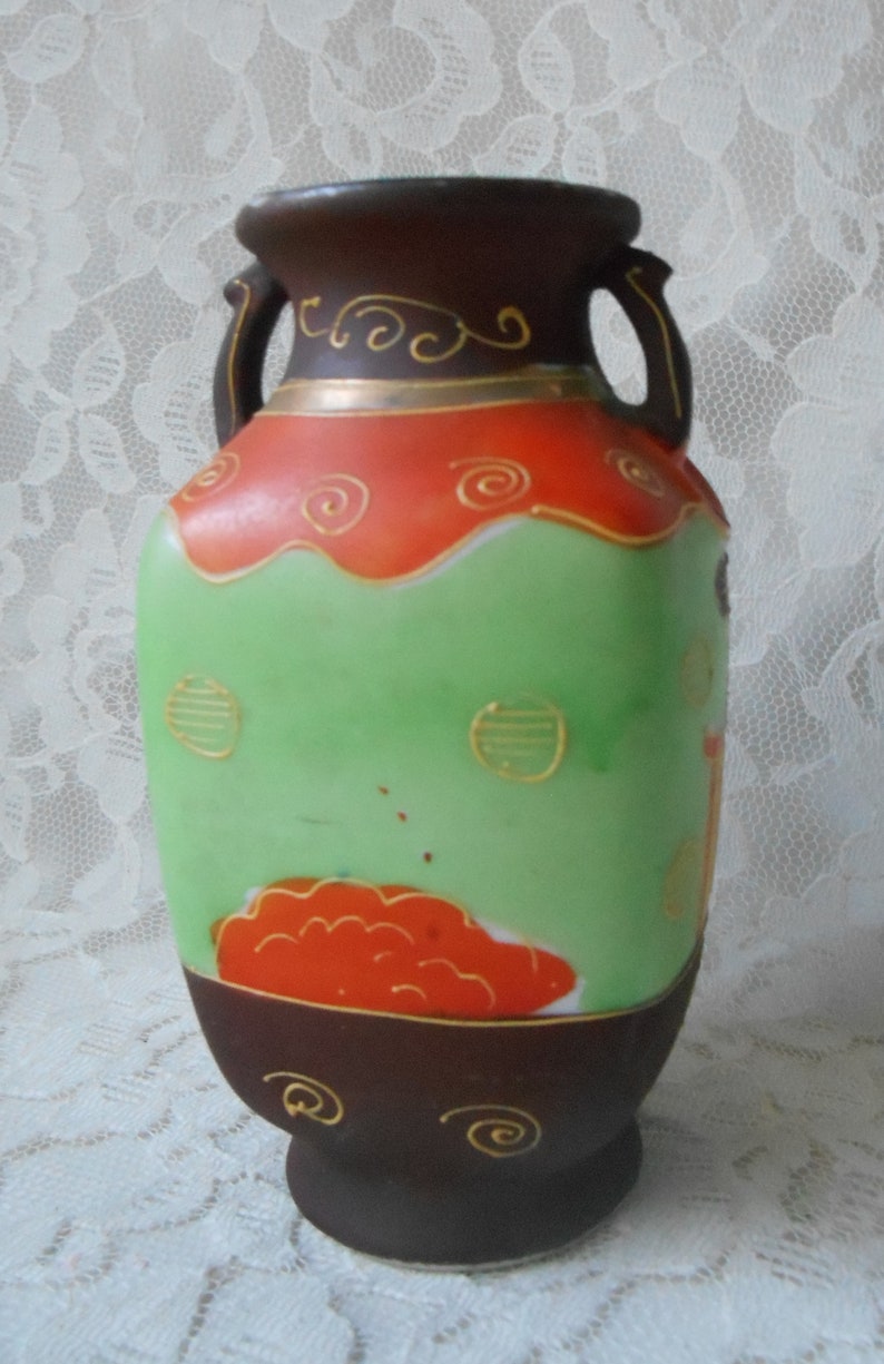 May include: A brown and green ceramic vase with gold accents and a red and orange floral design. The vase has two handles and a rounded base.