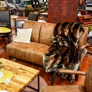 Puede incluir: Un sof&aacute; de cuero marr&oacute;n con una manta de piel sint&eacute;tica marr&oacute;n. El sof&aacute; tiene un respaldo capiton&eacute; y est&aacute; sobre una alfombra. Hay una mesa de caf&eacute; de madera delante del sof&aacute;.