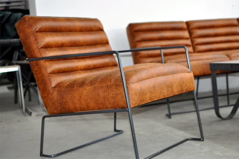 May include: Two brown leather chairs with black metal frames. The chairs have a tufted design and are set on a concrete floor.