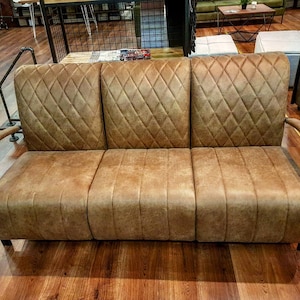 Puede incluir: Un sof&aacute; de cuero marr&oacute;n con un respaldo capiton&eacute; con forma de diamante y brazos de metal. El sof&aacute; est&aacute; sobre un suelo de madera.