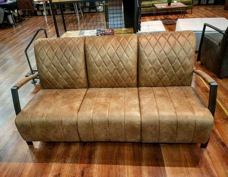 Puede incluir: Un sof&aacute; de cuero marr&oacute;n con un respaldo capiton&eacute; con forma de diamante y brazos de metal. El sof&aacute; est&aacute; sobre un suelo de madera.