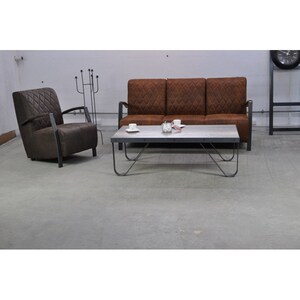 Puede incluir: Un sof&aacute; de cuero marr&oacute;n con tapicer&iacute;a de rombos y un sill&oacute;n a juego. Una mesa de centro de metal con tapa blanca se encuentra frente al sof&aacute;.