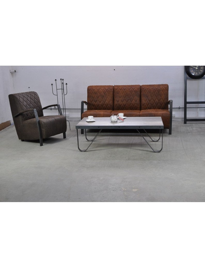 Puede incluir: Un sof&aacute; de cuero marr&oacute;n con tapicer&iacute;a de rombos y un sill&oacute;n a juego. Una mesa de centro de metal con tapa blanca se encuentra frente al sof&aacute;.