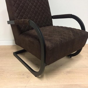 Puede incluir: Un sill&oacute;n acolchado marr&oacute;n con estructura de metal negro. El sill&oacute;n tiene un respaldo y brazos curvos, y la estructura est&aacute; hecha de una sola pieza de metal que forma un bucle continuo.