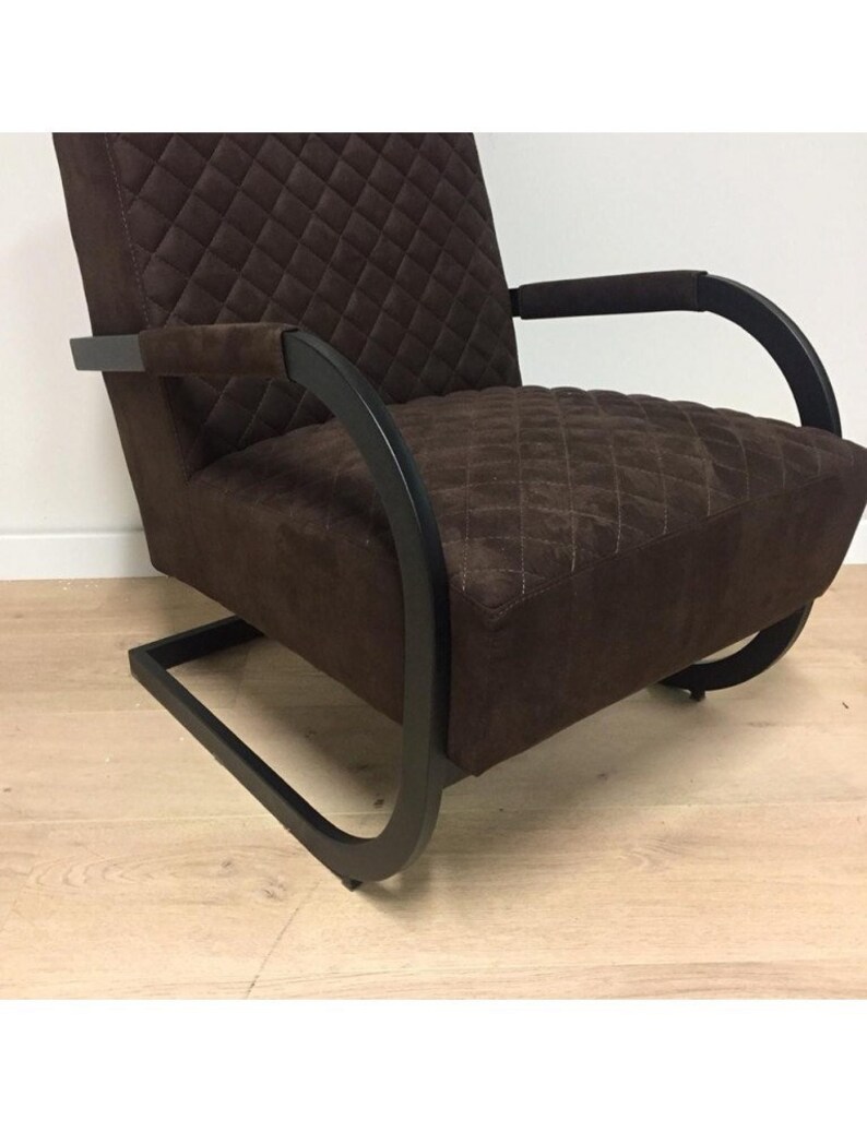 Puede incluir: Un sill&oacute;n acolchado marr&oacute;n con estructura de metal negro. El sill&oacute;n tiene un respaldo y brazos curvos, y la estructura est&aacute; hecha de una sola pieza de metal que forma un bucle continuo.