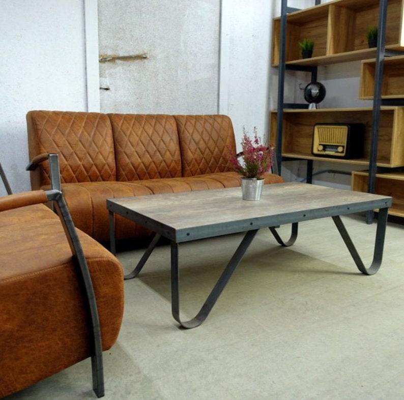 Puede incluir: Un sof&aacute; de cuero marr&oacute;n con una mesa de caf&eacute; de madera y metal delante. La mesa de caf&eacute; tiene una tapa gris y patas de metal negro. Hay una estanter&iacute;a detr&aacute;s del sof&aacute;.