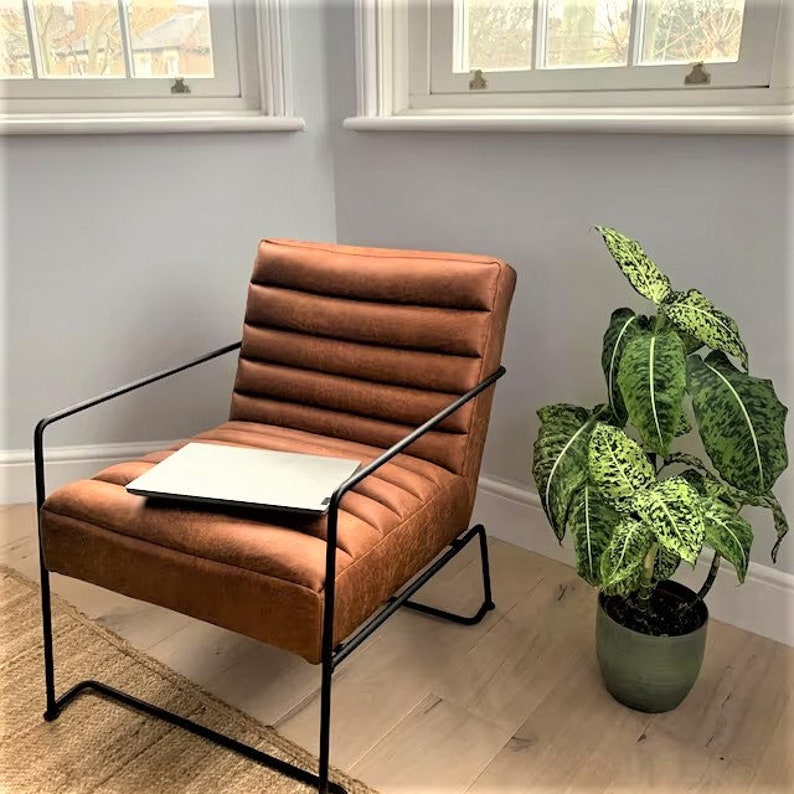 May include: A brown leather armchair with a black metal frame and a laptop on the seat. A potted plant with green and white leaves is in the corner of the room.