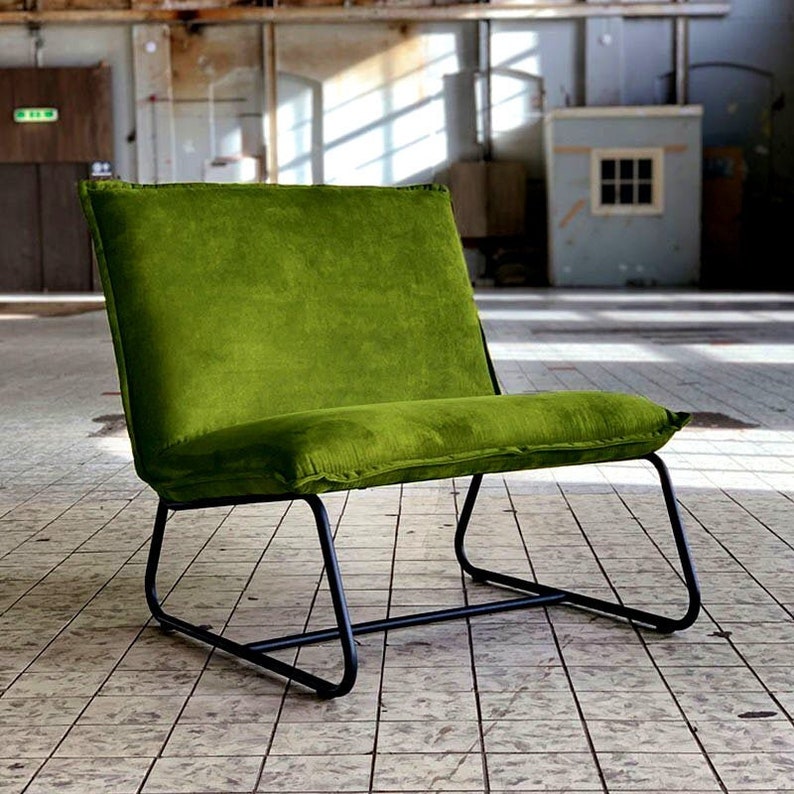 Puede incluir: Un sill&oacute;n de terciopelo verde con un marco de metal negro. El sill&oacute;n est&aacute; sentado en un suelo de baldosas.
