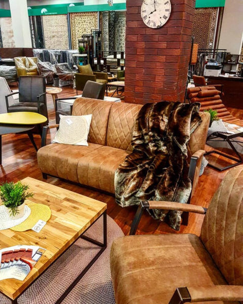 Puede incluir: Un sof&aacute; de cuero marr&oacute;n con una manta de piel sint&eacute;tica marr&oacute;n. El sof&aacute; tiene un respaldo capiton&eacute; y est&aacute; sobre una alfombra. Hay una mesa de caf&eacute; de madera delante del sof&aacute;.