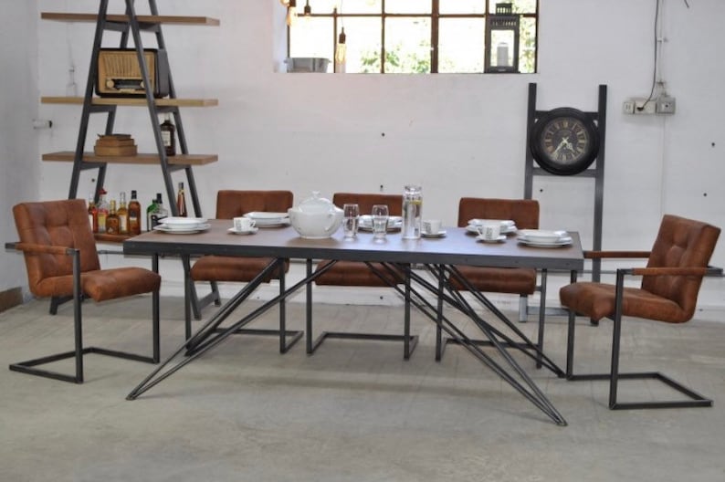 May include: A rustic dining table with a dark wood top and a metal frame. The table is surrounded by six brown leather chairs with metal frames. The table is set with plates, glasses, and a teapot.