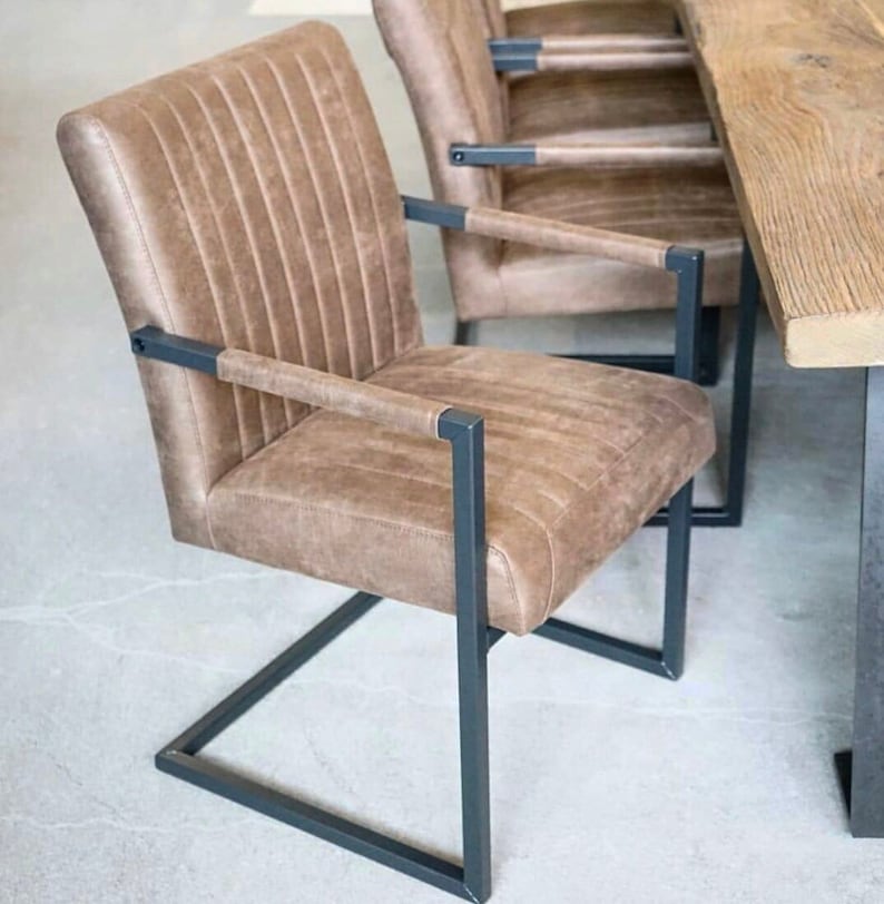 May include: A brown leather dining chair with a metal frame. The chair has a square back and a curved seat. The chair is on a light grey floor.