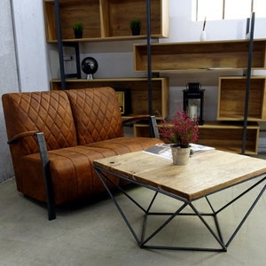 Puede incluir: Un sof&aacute; de cuero marr&oacute;n de dos plazas con tapicer&iacute;a de rombos y brazos de metal se encuentra frente a una estanter&iacute;a de madera. Una mesa de caf&eacute; geom&eacute;trica con una tapa de madera se encuentra frente al sof&aacute;.