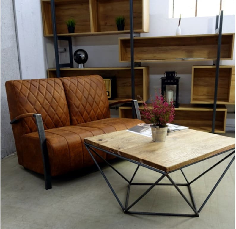 Puede incluir: Un sof&aacute; de cuero marr&oacute;n de dos plazas con tapicer&iacute;a de rombos y brazos de metal se encuentra frente a una estanter&iacute;a de madera. Una mesa de caf&eacute; geom&eacute;trica con una tapa de madera se encuentra frente al sof&aacute;.