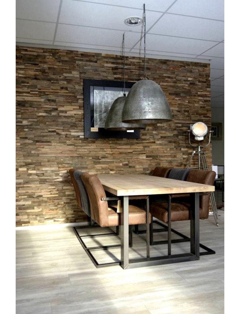 May include: A rustic wooden wall with a reclaimed wood paneling design. A wooden table with a metal frame sits in front of the wall. The table is surrounded by six chairs with brown leather seats. Three pendant lights hang from the ceiling above the table.