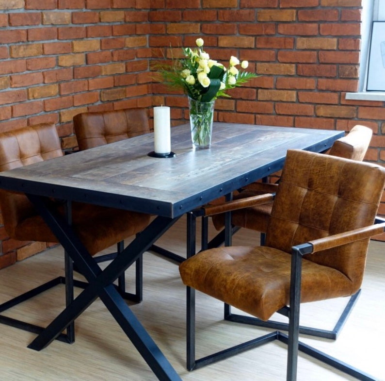 May include: A rustic dining table with a wood top and black metal legs. Four chairs with brown leather upholstery surround the table. A vase with white flowers sits on the table.