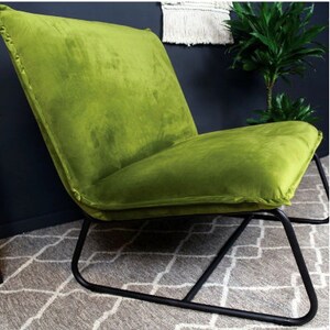 Puede incluir: Un sill&oacute;n de terciopelo verde con estructura de metal negro. El sill&oacute;n tiene un perfil bajo y un asiento ancho.