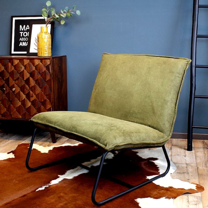 Puede incluir: Un sill&oacute;n tapizado en verde con un marco de metal negro se encuentra sobre una alfombra de piel de vaca marr&oacute;n y blanca. El sill&oacute;n tiene un respaldo alto y un asiento ancho.