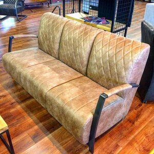 Puede incluir: Un sof&aacute; de cuero marr&oacute;n con un patr&oacute;n de rombos y brazos de metal negro. El sof&aacute; est&aacute; sentado en un suelo de madera.