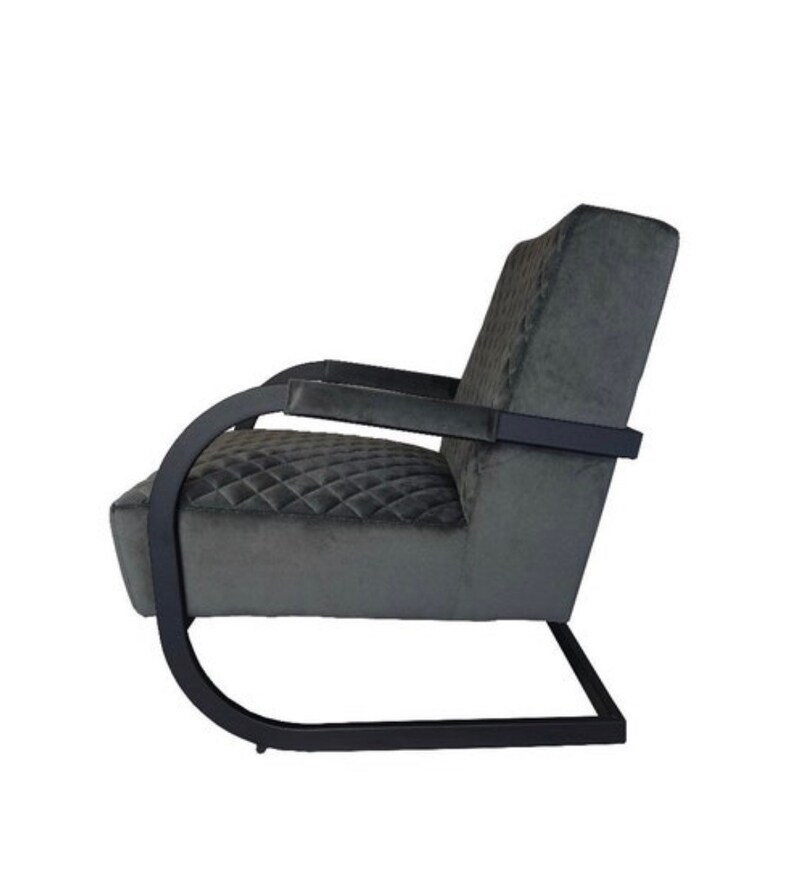 Puede incluir: Un sill&oacute;n negro con tapicer&iacute;a de terciopelo gris acolchado y estructura de metal negro. El sill&oacute;n tiene un respaldo y brazos curvos.