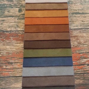 Puede incluir: Un muestrario de 15 muestras de tela en varios colores, incluyendo beige, marr&oacute;n, naranja, verde, azul y gris. Las muestras de tela est&aacute;n dispuestas en una fila vertical sobre un fondo de madera.