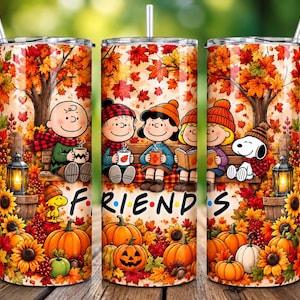 Könnte beinhalten: Ein zylindrischer Edelstahlbecher mit einer farbenfrohen Herbstszene, die Peanuts-Figuren auf einer Bank zeigt, umgeben von fallenden orangefarbenen und roten Ahornblättern, Sonnenblumen und Kürbissen. Das Wort FRIENDS ist in Schwarz aufgedruckt.