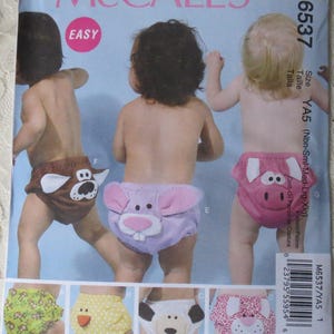 May include: McCall's sewing pattern M6537 for baby cloth diapers. The pattern features various animal designs, including a dog, pig, and bunny. The cover shows babies wearing the diapers. The word "EASY" is in a pink circle.