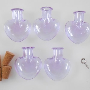 May include: Five small, lavender glass heart-shaped bottles with cork stoppers. The bottles are arranged in a row with two on the left and three on the right. There are also four silver eye hooks and four cork stoppers.